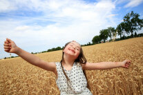 Mädchen steht in Getreidefeld und streckt Hände seitlich aus 