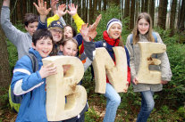 Mehrere Kinder im Wald, die Buchstaben B, N und E halten