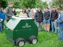 Eine Menschengruppe betrachtet einen grünen, kastenförmigen Roboter
