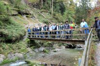 EIne Gruppe von Menschen steht auf einer Brücke über einen Bach