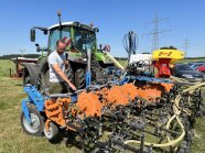 Mann mit Mikro vor landwirtschaftlichem Gerät mit Traktor