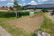 Erdige Fläche vor landwirtschaftlichem Betrieb, in der Mitte steckt ein Schild